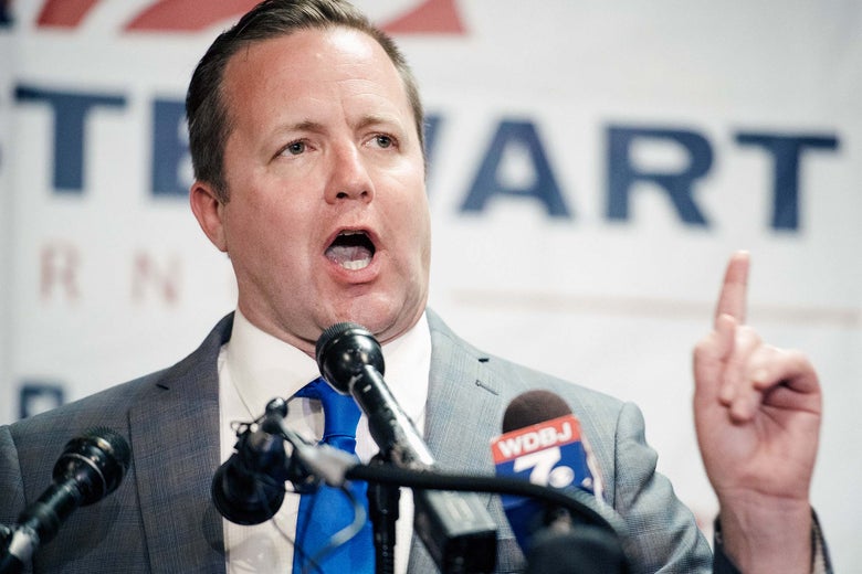 Stewart speaks in front of an array of microphones while wagging his finger.